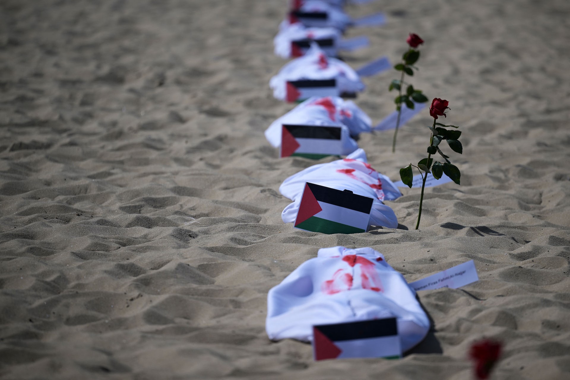 cobertores brancos com tinta vermelha ao lado de bandeiras palestinas em uma praia.