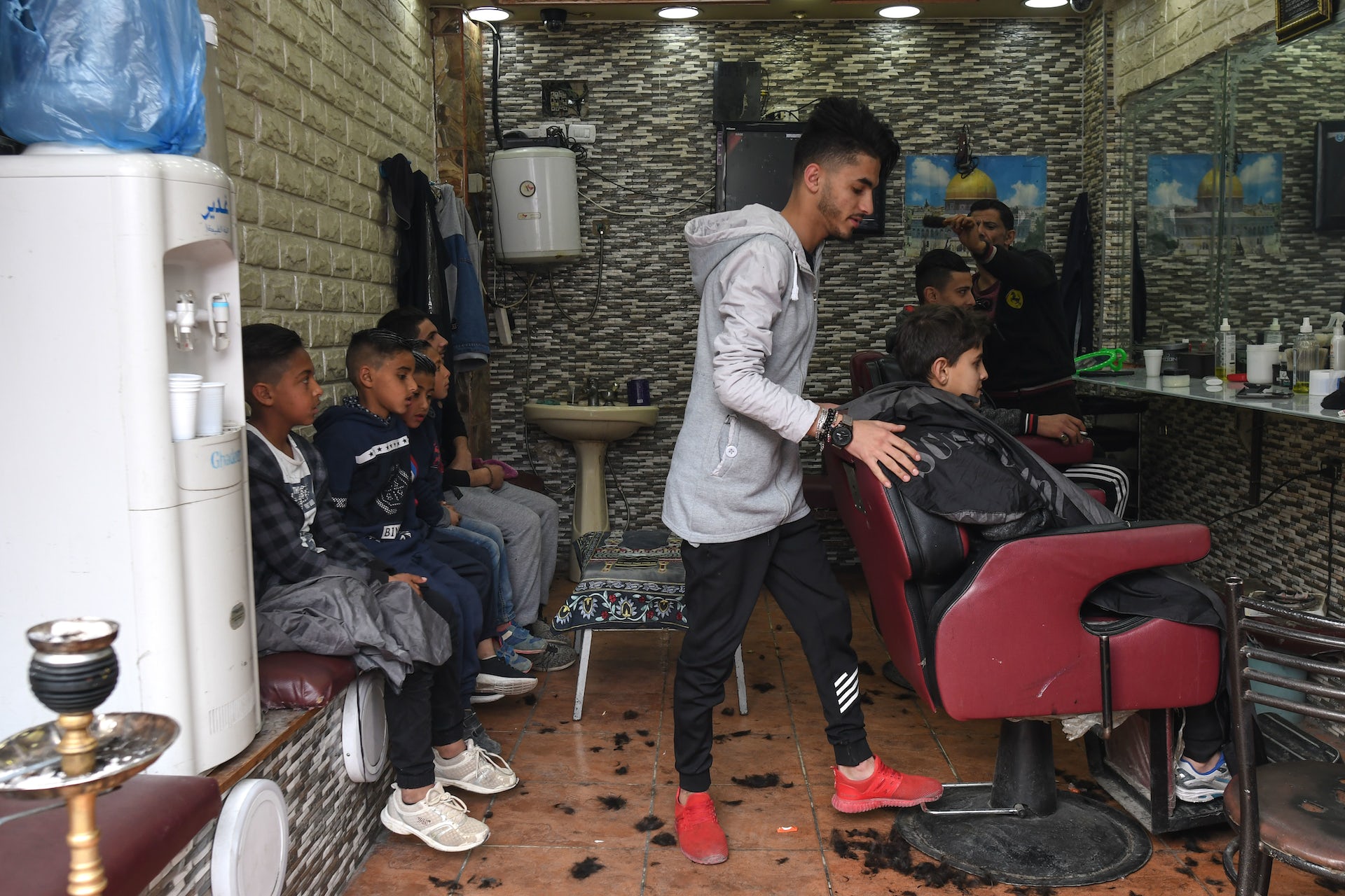 Um jovem barbeiro recebe uma criança sentada em uma cadeira enquanto várias outras esperam.